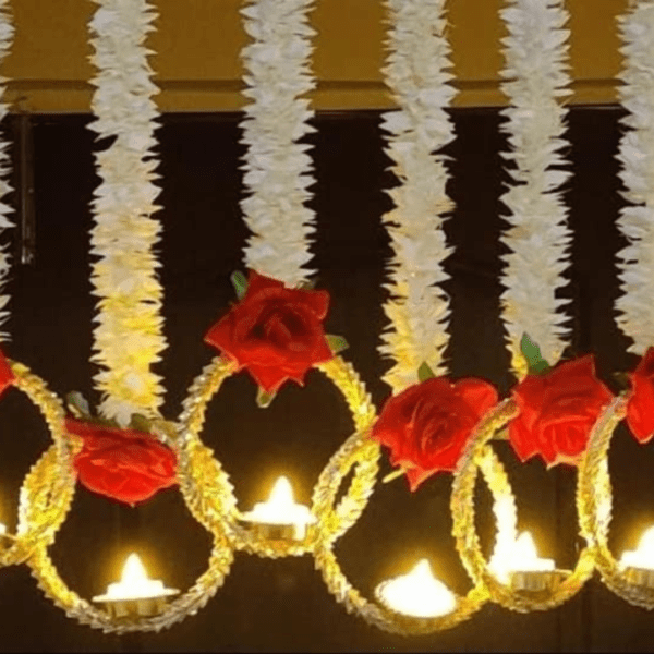 During Diwali, Torans are hung across doorways as a symbol of welcome and prosperity. These decorative pieces are usually made with vibrant marigold flowers, auspicious gajra leaves, and delicate rose and ring. Traditional Diwali decorations include lights, diyas (oil lamps made from clay), flowers (like these marigold garlands), torans (decorative door hangings), and rangoli, a type of intricate art crafted by flowers. One Box contains 5 Pieces of Elegant Artificial Flower String with LED Lamps /Diya. Product exactly as shown in Image. Length of White flowers is 3 Ft / 36 Inches . Total length of each string is approx 42 Inches. Attractive Roses attached on hanging are Red and made of Velvet. Ring Size below hanging is big and gives attractive look to wall / door decor.